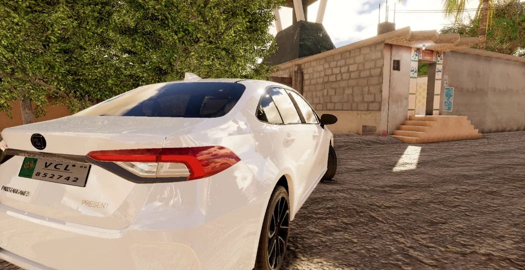 A white sedan driving through a sunlit village street
